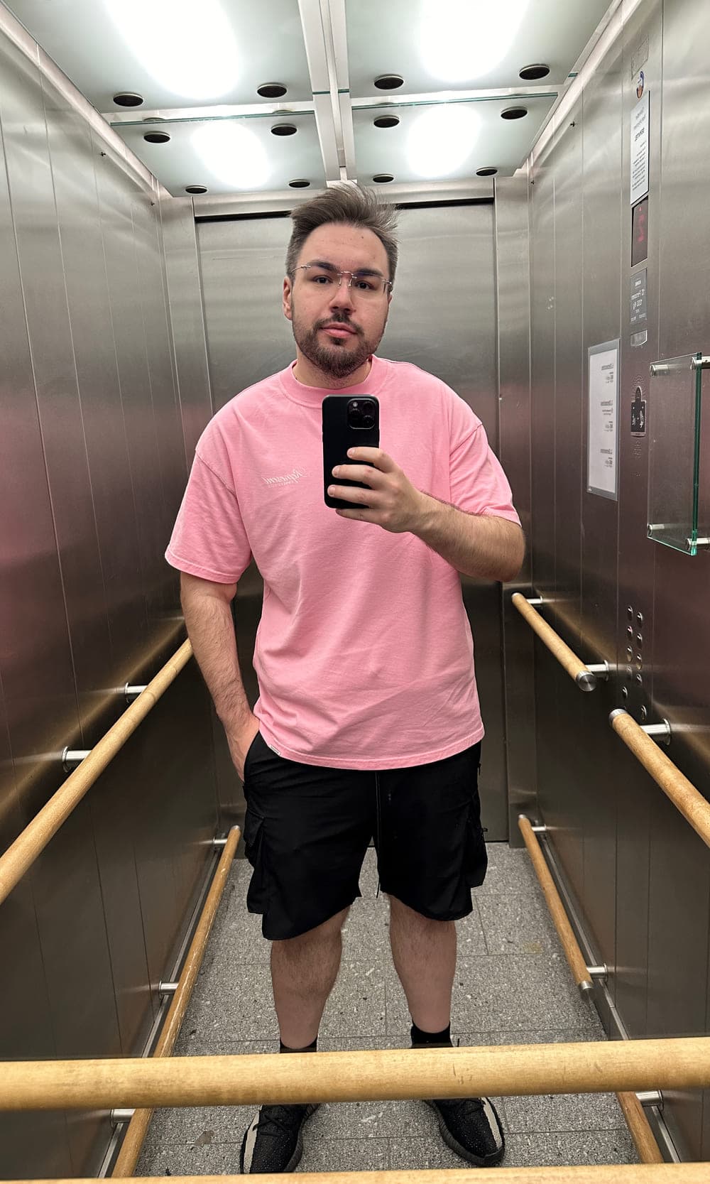 Dennis heute: Spiegel-Selfie im Aufzug, rosa T-Shirt und kurze Hose